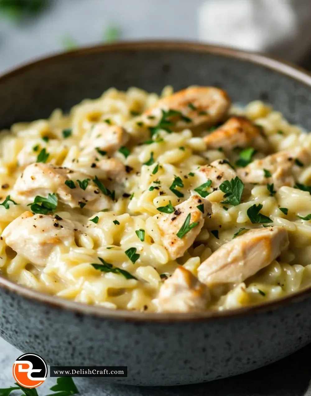 Creamy orzo with chicken served in a bowl, garnished with herbs.