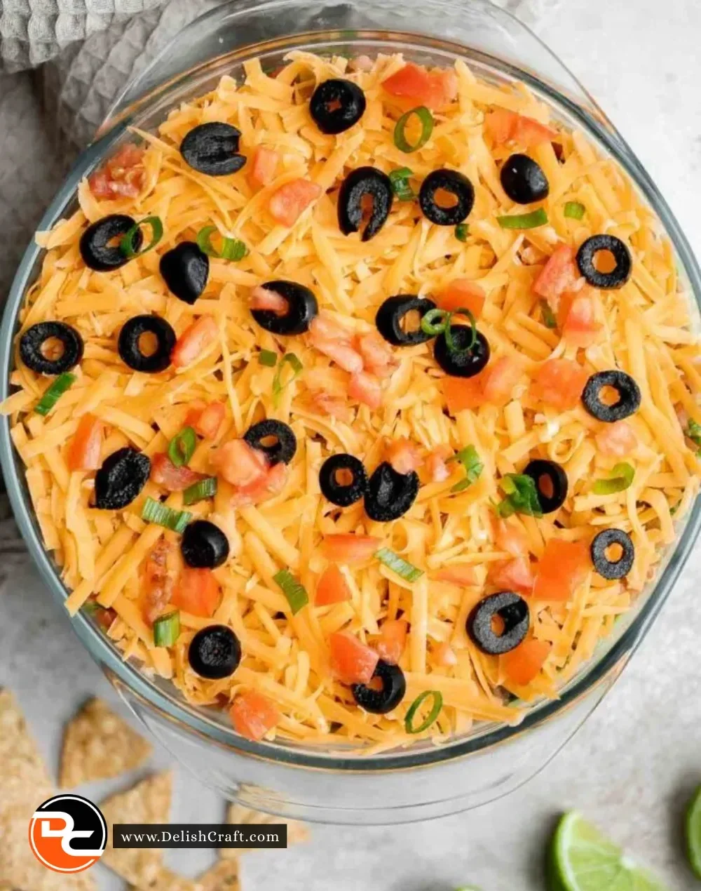 A colorful 7 Layer Dip served in a glass dish, showcasing layers of beans, guacamole, sour cream, and salsa.