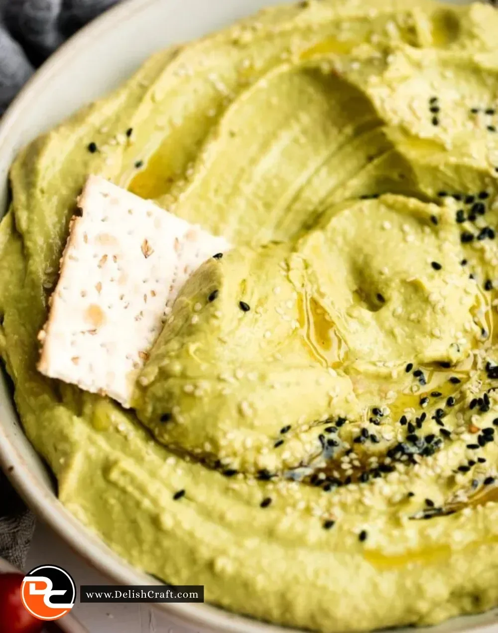 Bowl of creamy avocado hummus surrounded by fresh vegetables and pita bread.