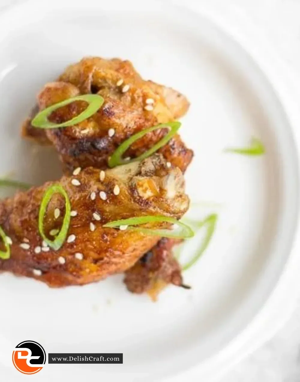 Plate of crispy Baked Asian Chicken Wings garnished with green onions and sesame seeds.