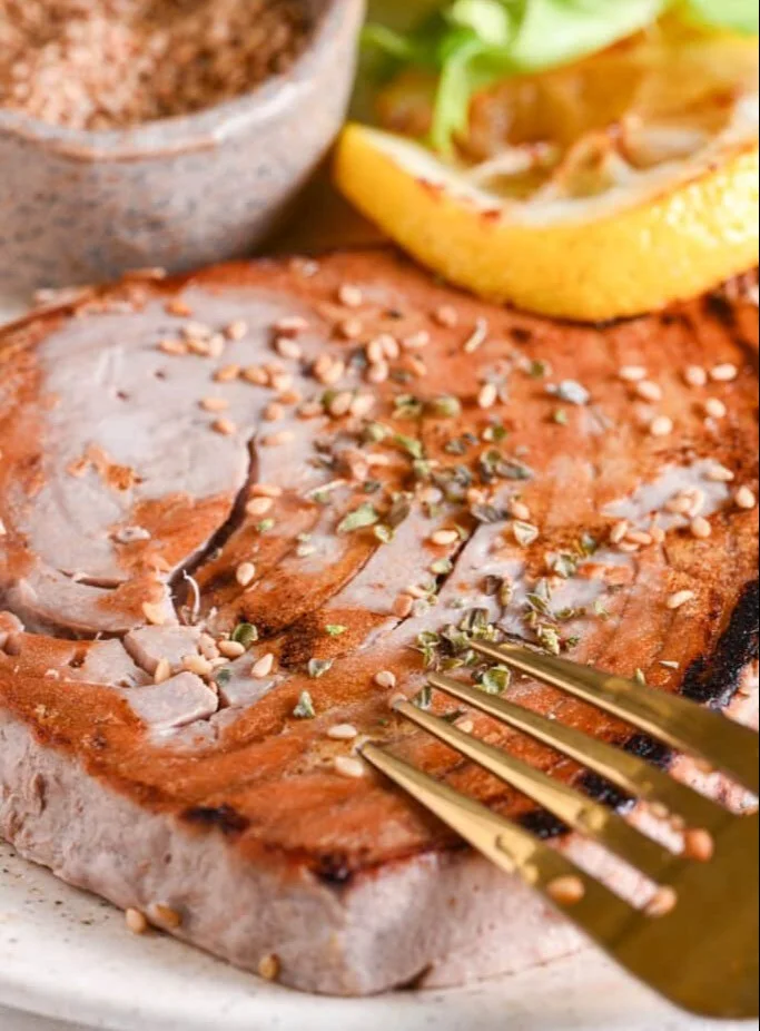 Grilled tuna steak garnished with herbs and served with lemon slices.