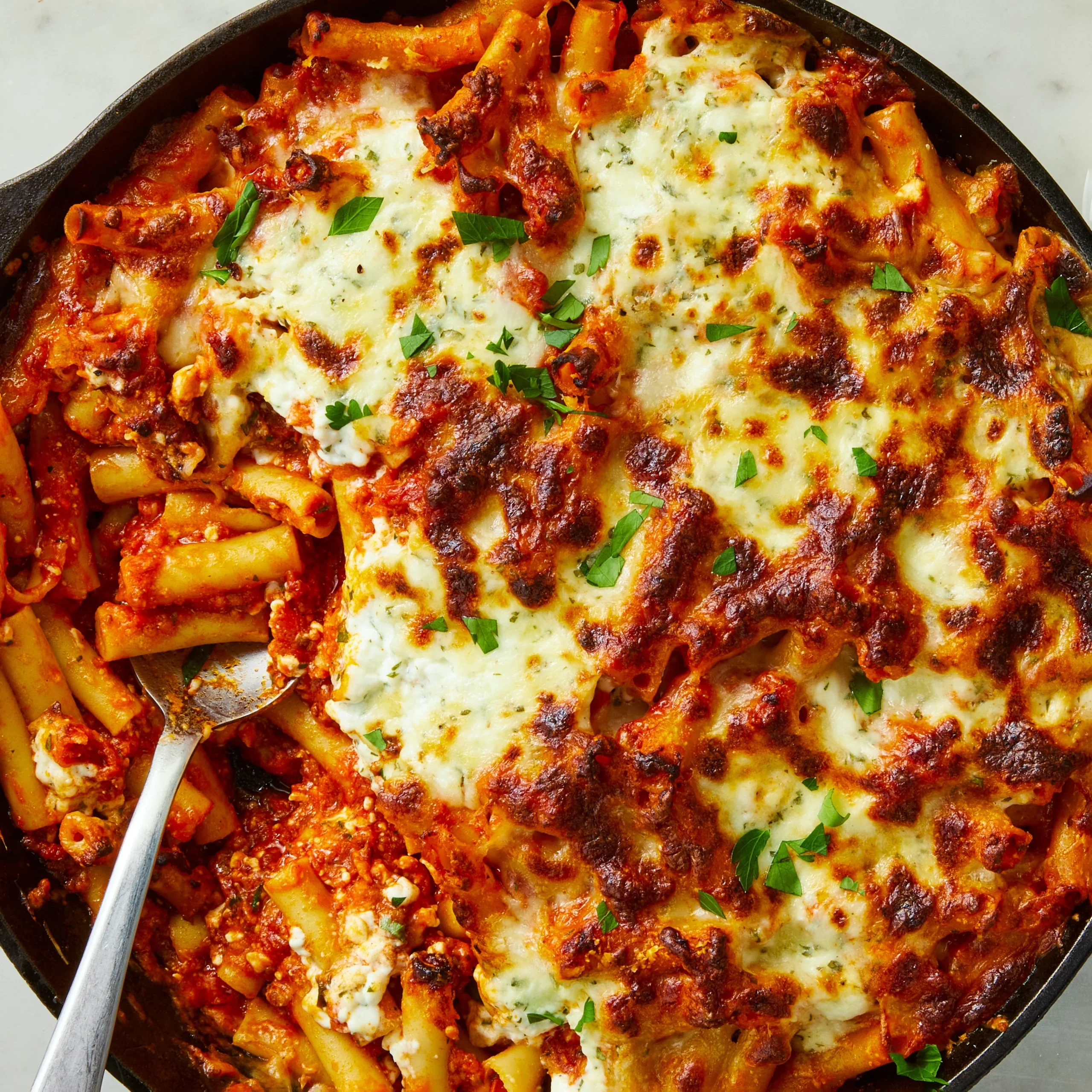 Baked ziti with cottage cheese in a ceramic dish garnished with parsley